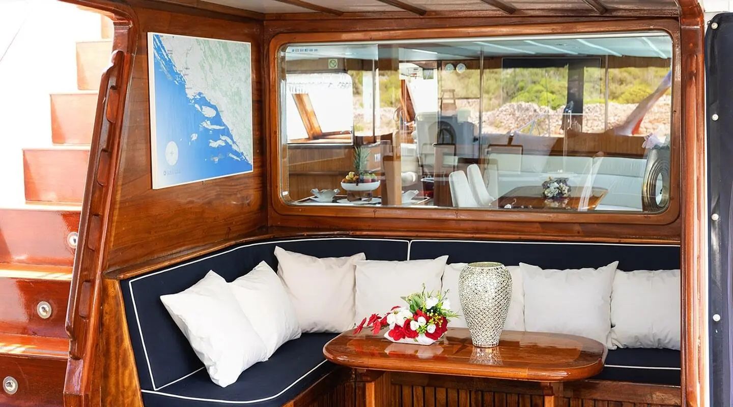 Wooden aft deck seating area with white cushions and decorative vase on table