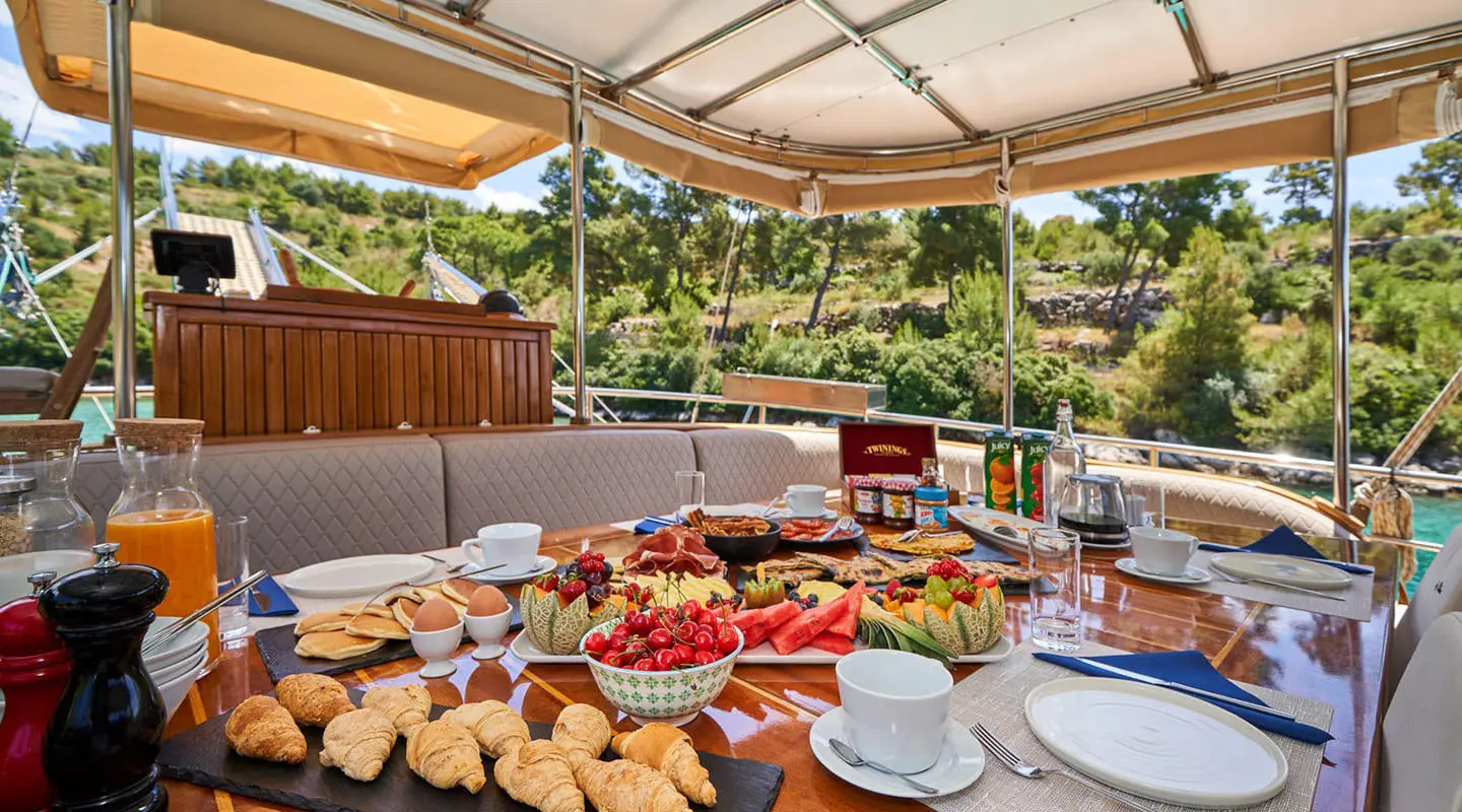Luxurious yacht Libra dining table set with bread, fruits, and pastries aboard under canopy