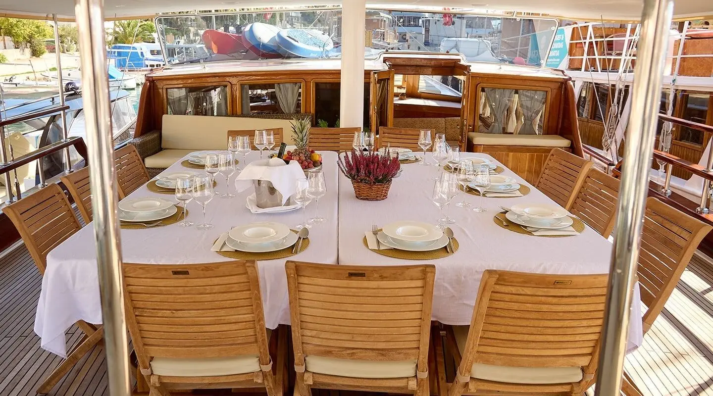 Linda yacht dining table on deck with white table setting and wooden chairs