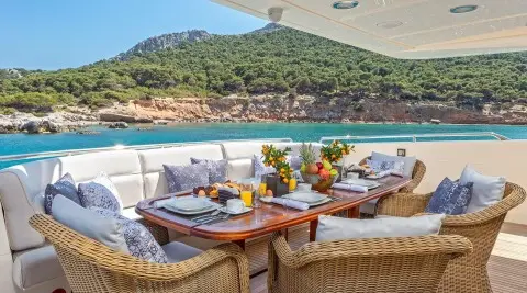Divine yacht dining setup on deck at sunset with wooden tables and wicker chairs