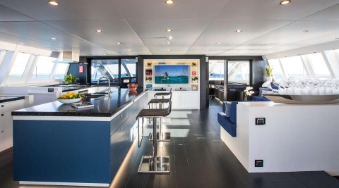 Cartouche luxury yacht interior: modern galley with blue cabinetry, marble-like countertop, bar seating, and sea-view salon