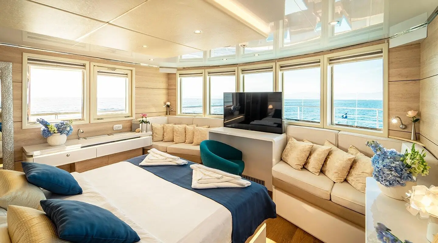 Interior of Riva yacht with large windows, cream sofas, bed, and flat screen TV