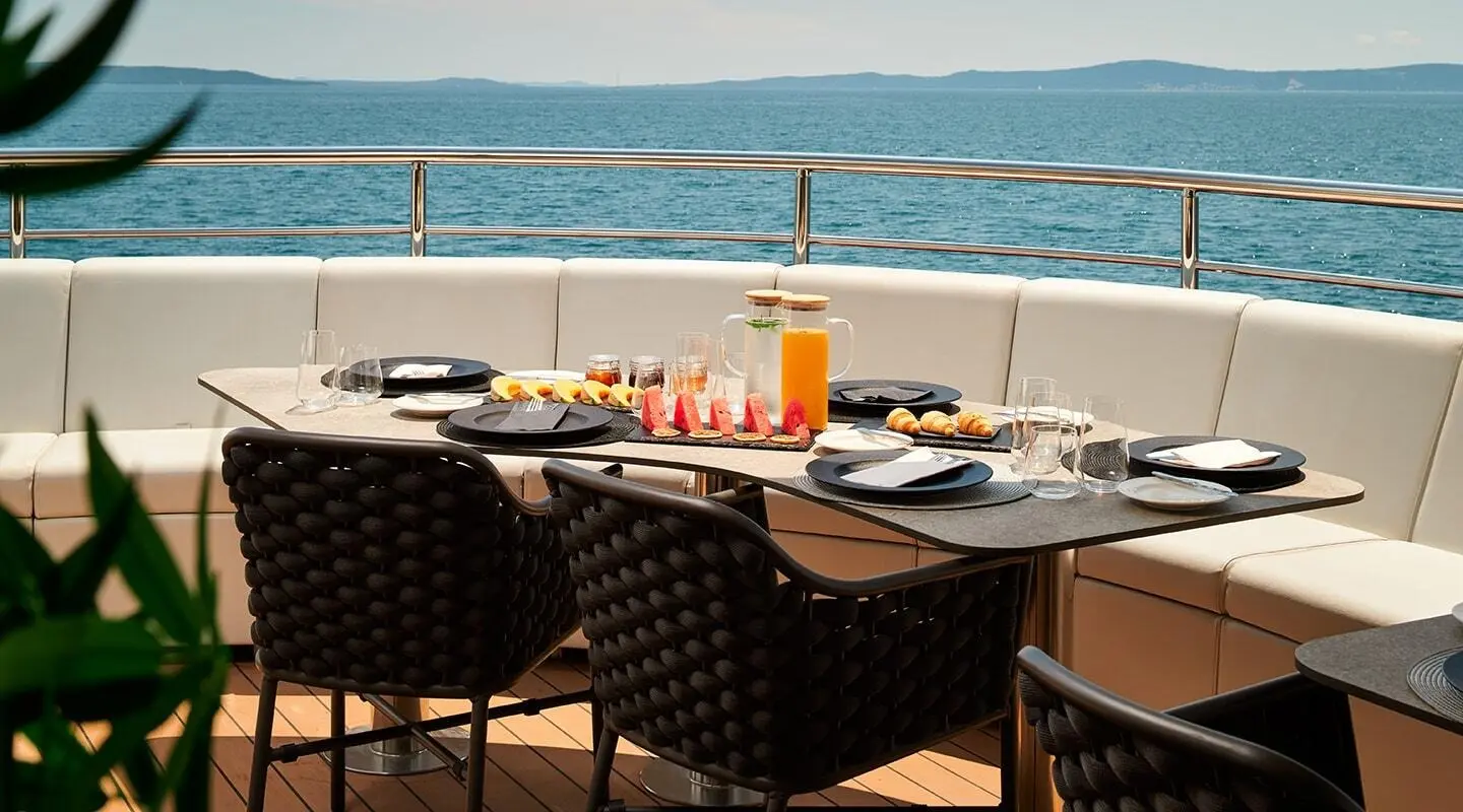 Ohana yacht dining setup on deck with plates, drinks, and sea view