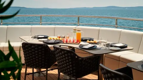 Ohana yacht dining setup on deck with plates, drinks, and sea view