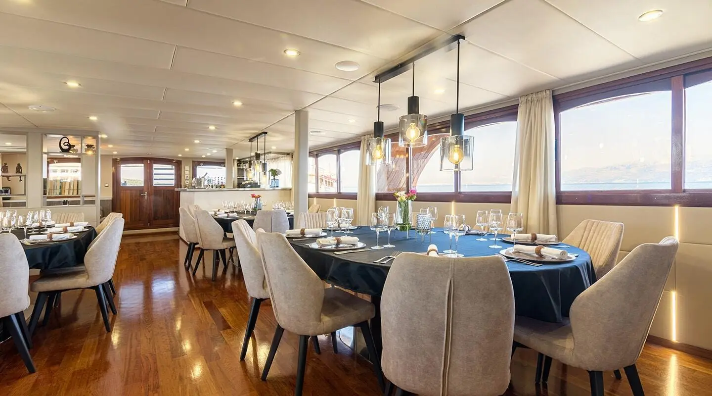 Luxurious yacht Melody dining area with a long table, pendant lights, and windows