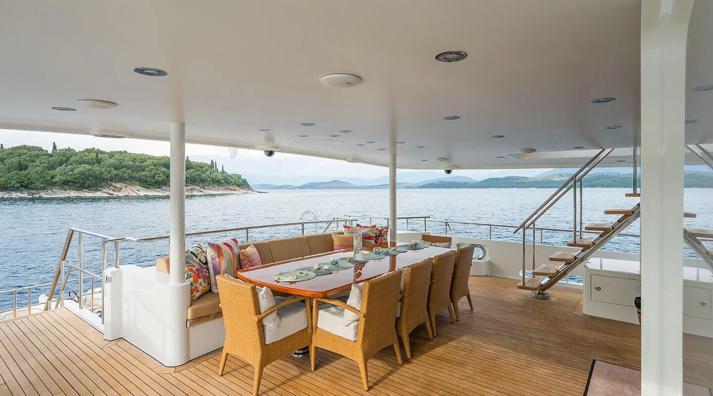 Serenity yacht dining deck with wooden table set for meals under awning