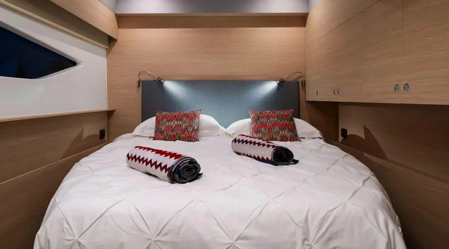 Two neatly made beds on a wooden yacht cabin with white bedding and red pillows