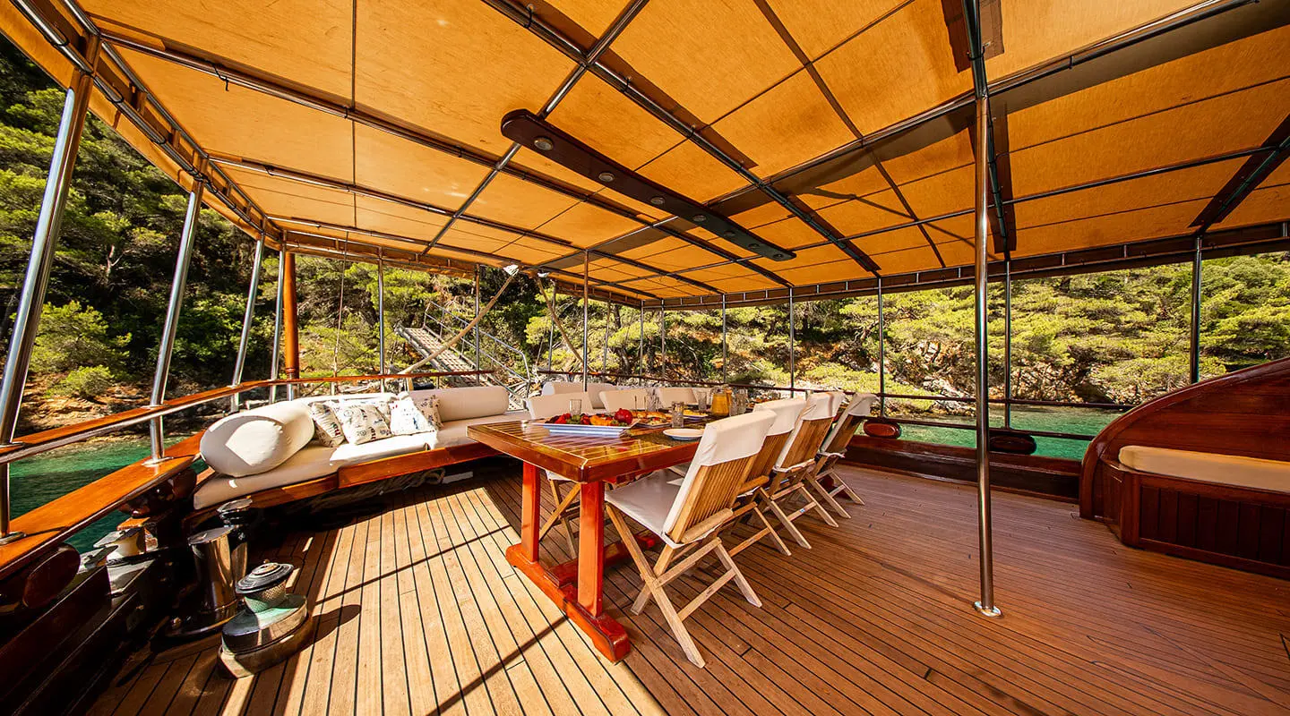 Aft deck of Gulet Eleganza with wooden table, benches, and shaded cabin area