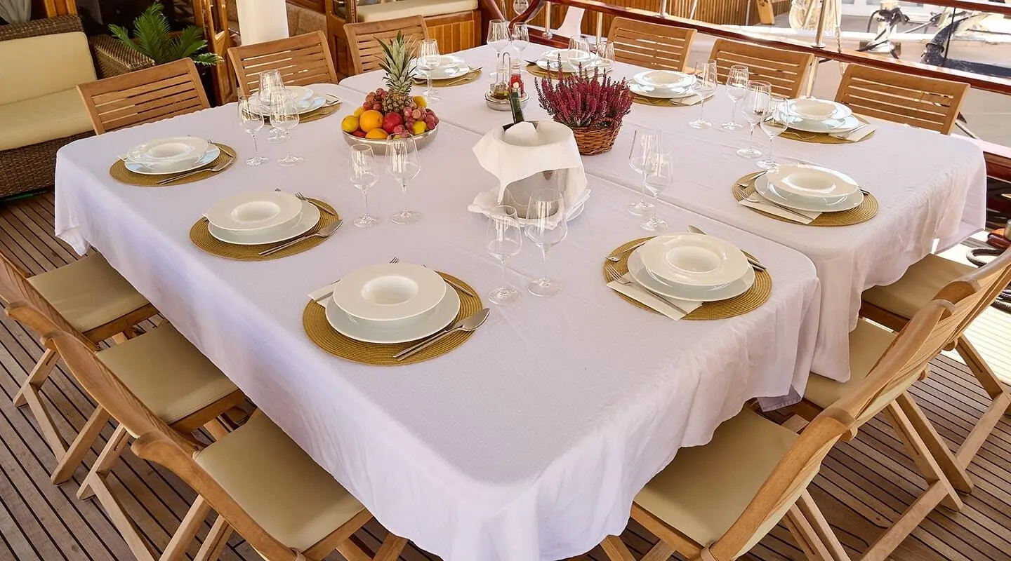 Yacht Linda dining table set with white tablecloth, plates, and glasses on deck at sunset