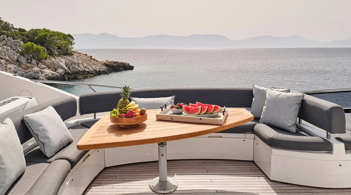 Yacht M Five on a sunlit deck with a wooden table and cushions by the sea
