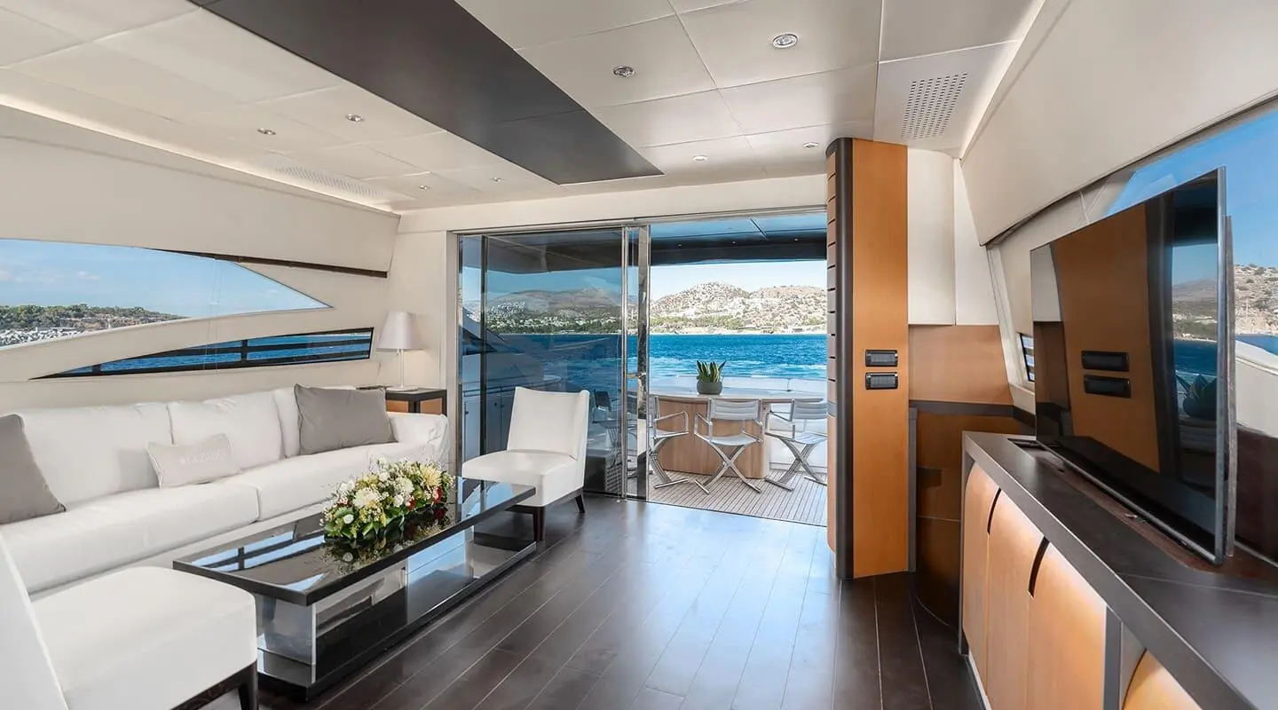 Interior yacht salon with seating, large windows, and a view of the sea at sunset