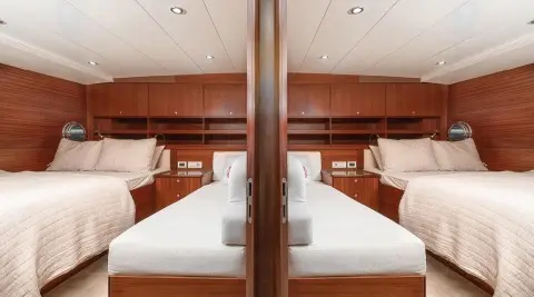 Interior view of a luxury yacht with twin cabins, wooden cabinetry, and neatly made beds