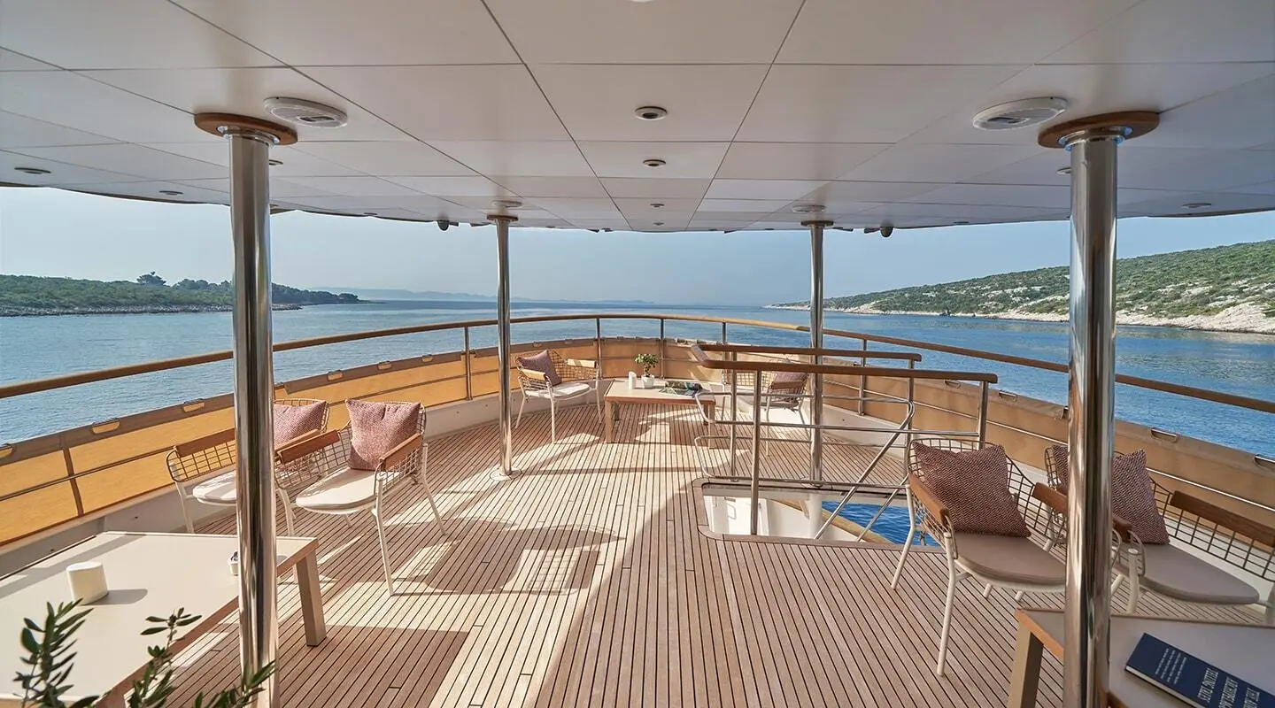 Aft deck of La Perla yacht with wood deck, seating, and railings over calm sea
