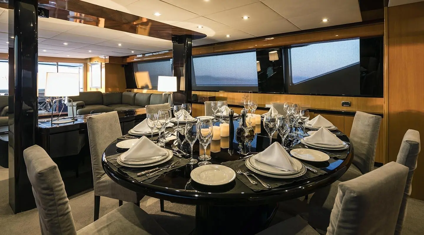 Interior dining area on a luxury yacht with a table set for dinner and large windows showing sunset