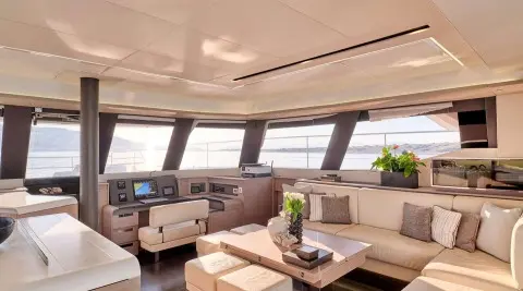 Luxurious yacht salon interior with beige seating, wooden table, and large windows