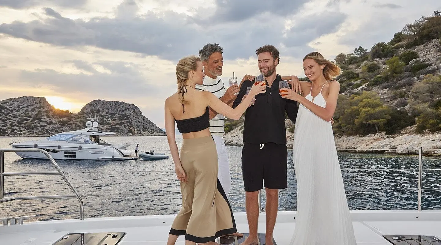 Daiquiri yacht in a picturesque cove with guests toasting on deck at sunset