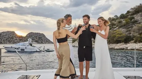 Daiquiri yacht in a picturesque cove with guests toasting on deck at sunset