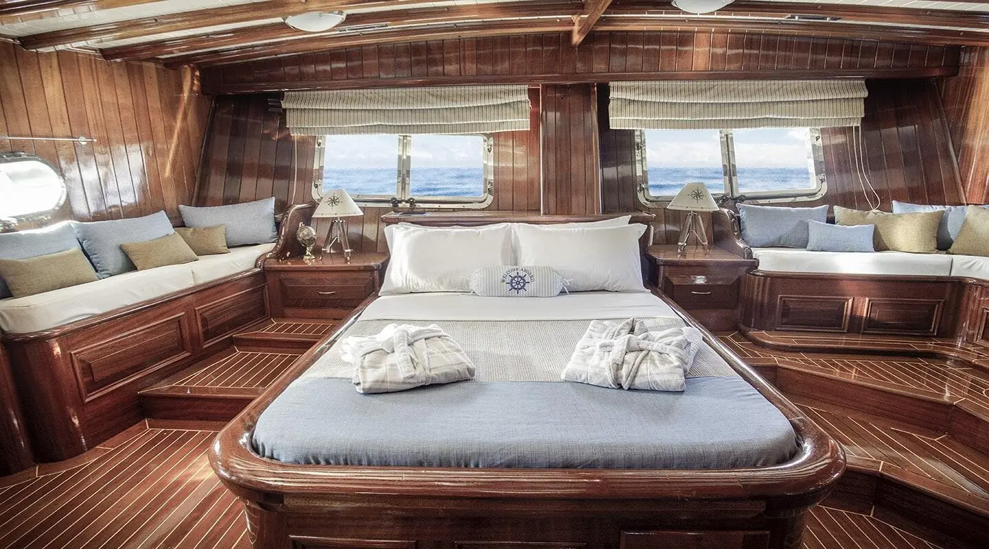 Gulet Entre Cielos master cabin with front-facing bed, wood deck, and porthole view