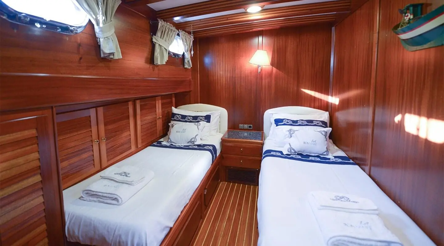 Two single beds inside a polished wooden cabin with portholes and bedding