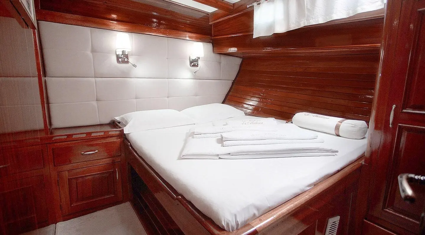 Malena yacht cabin with white bed, wooden paneling, soft lighting, compact space