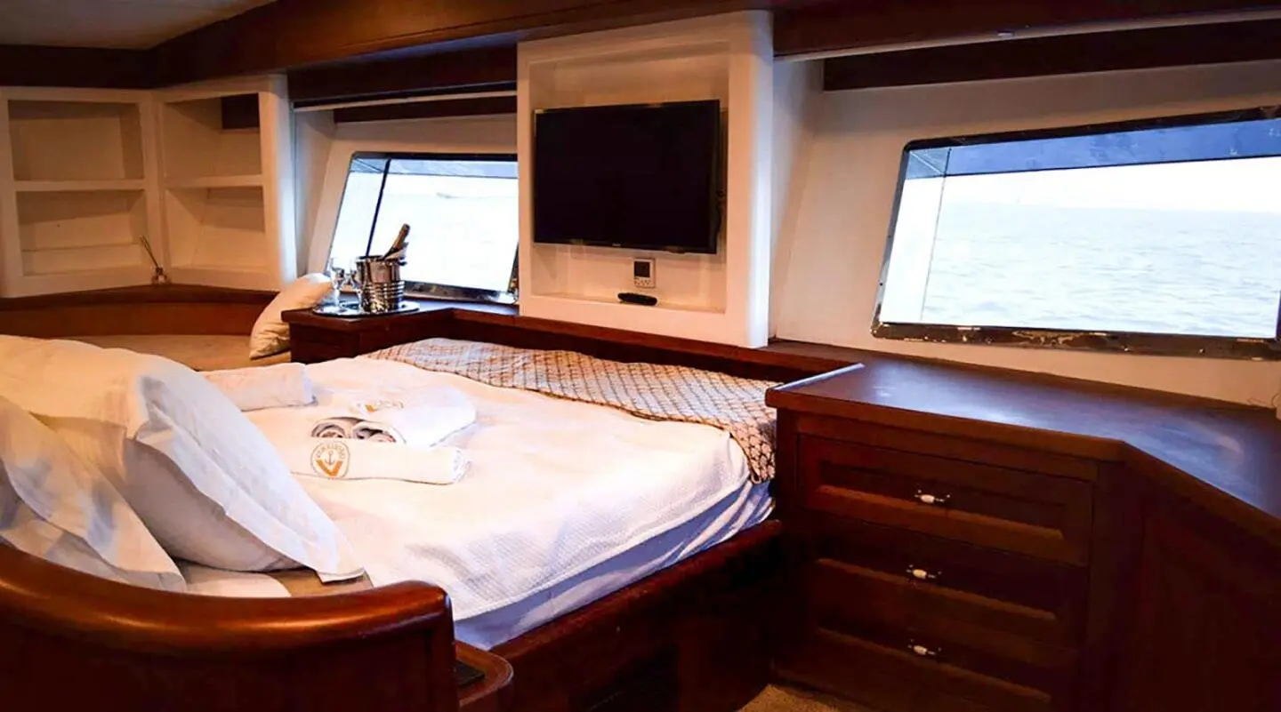 Virtuoso yacht interior with bed, wooden cabinetry, and windows at sunset