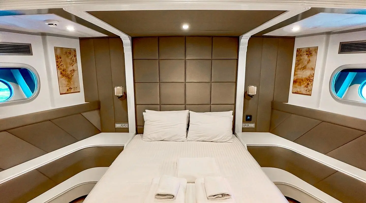 Angelo III yacht interior with a large bed, beige cushioned headboard, and pillows