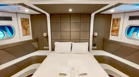 Angelo III yacht interior with a large bed, beige cushioned headboard, and pillows