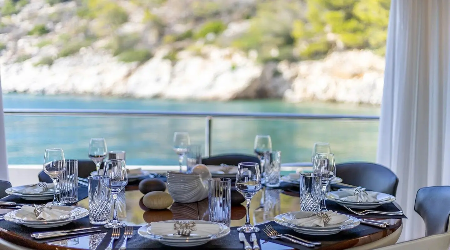 Vista yacht dining deck set for sunset with plates, glasses, and ocean view