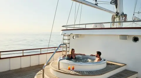 Yacht Corsario with people on a round dinghy near a luxurious deck at sunset