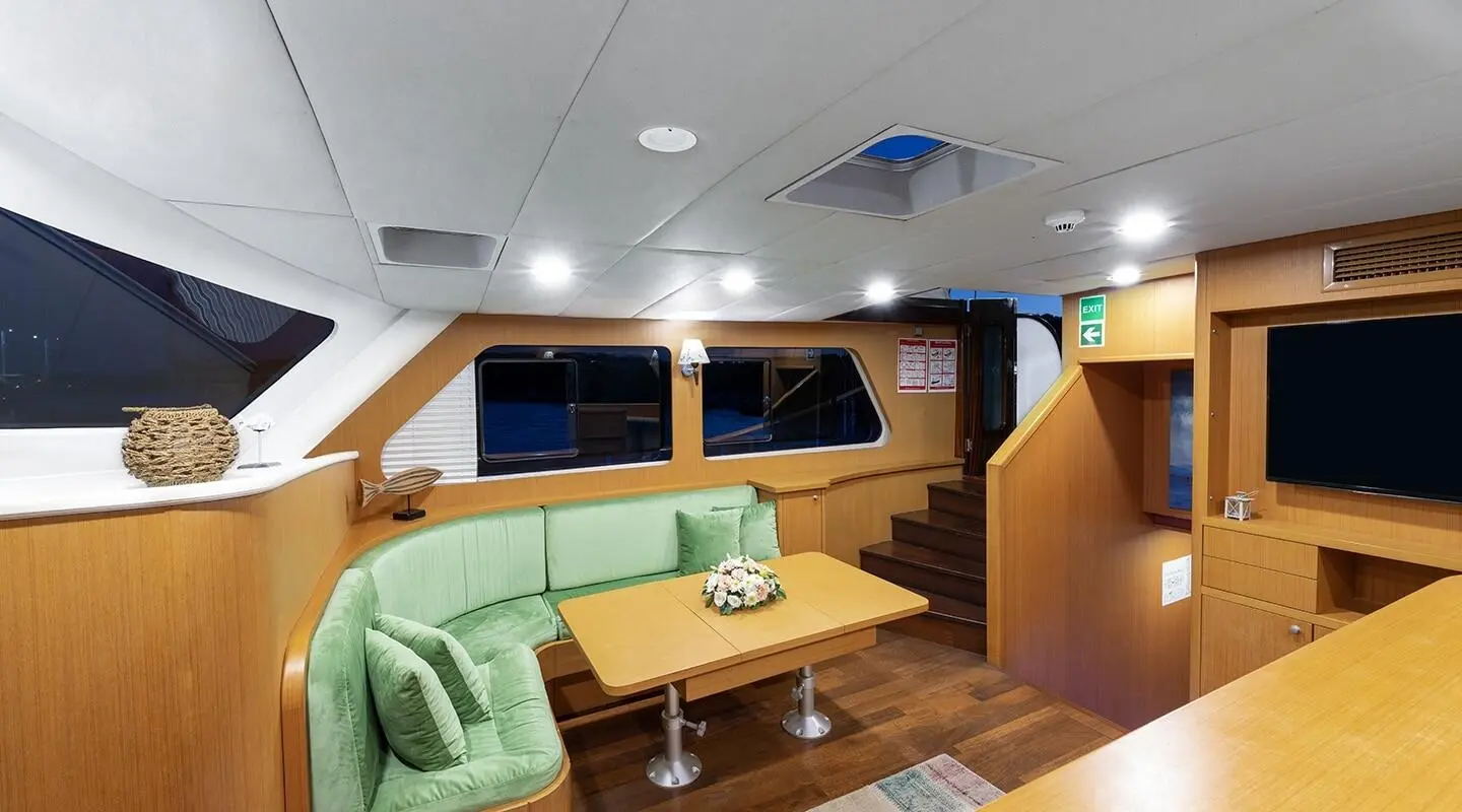 Wooden interior with a green upholstered seating area and wooden table in the yacht saloon