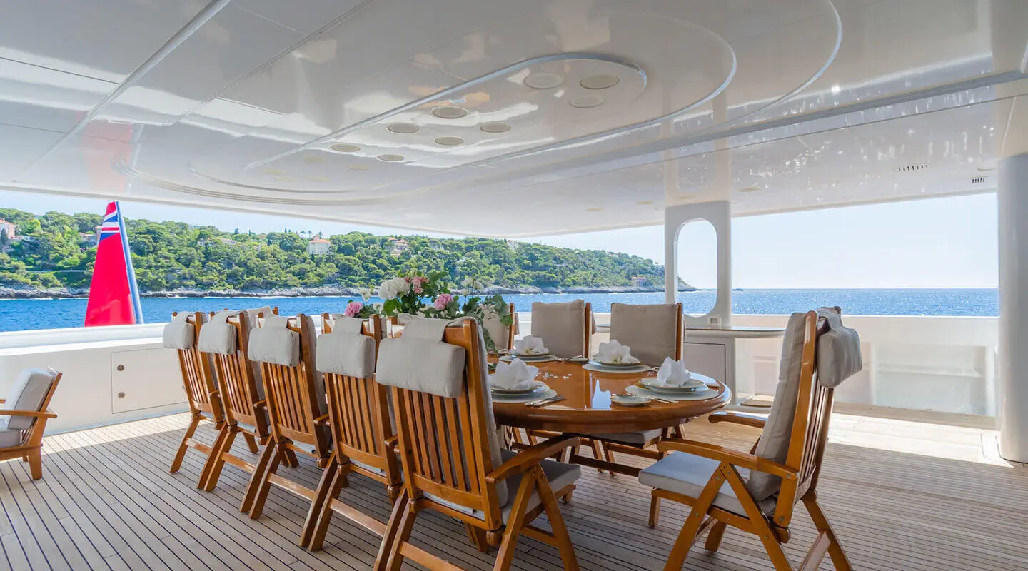 Apogee yacht dining area on deck with wooden chairs around a table