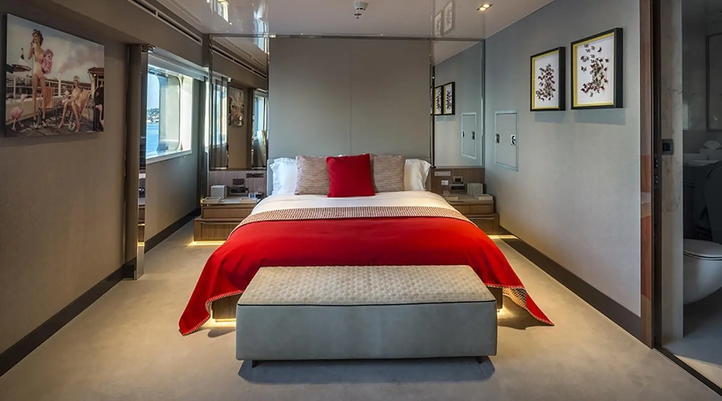 Bedroom aboard a yacht with a central bed, red throw blanket, and modern interior