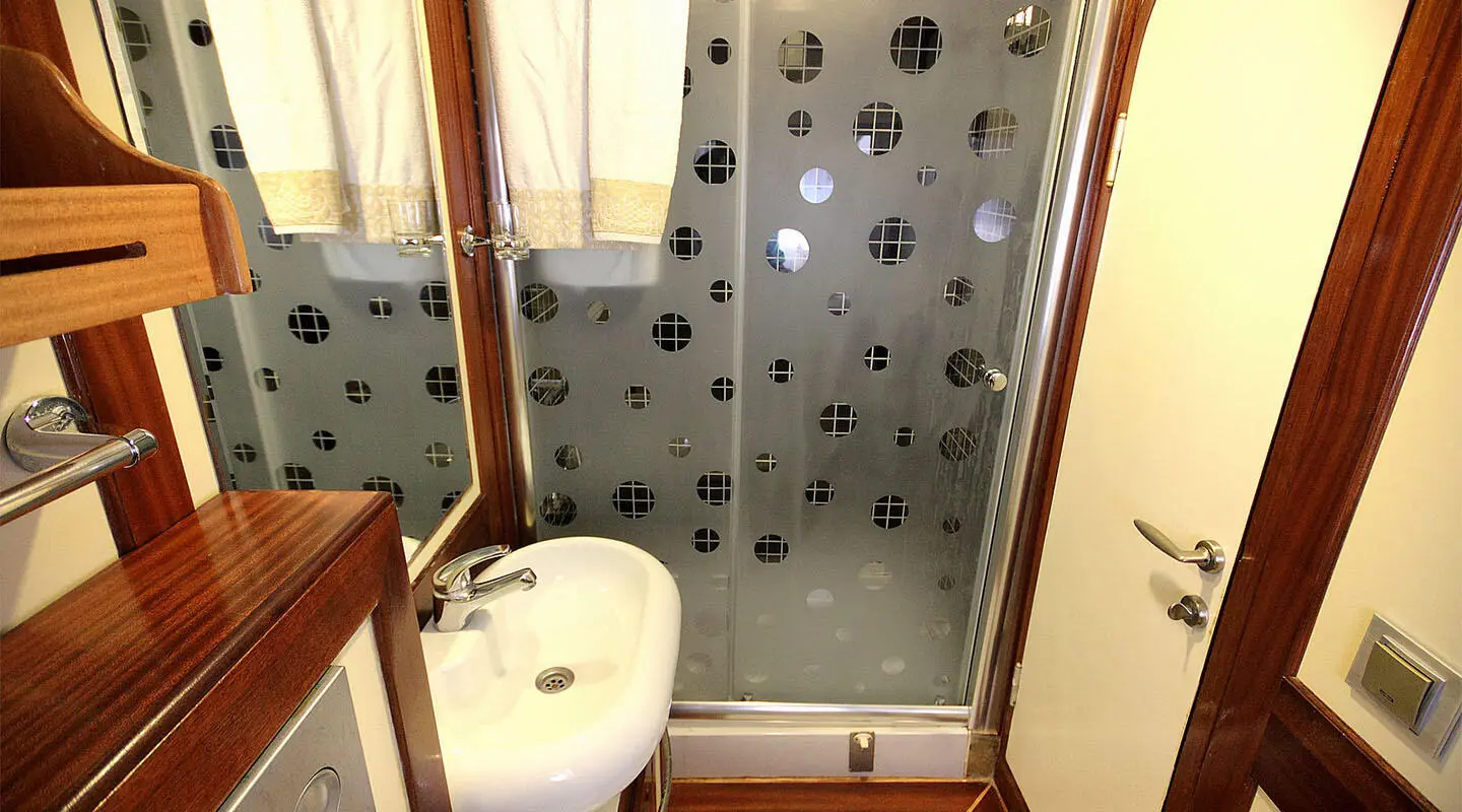 Small white sink with wooden cabinet and a glass shower enclosure in a yacht bathroom
