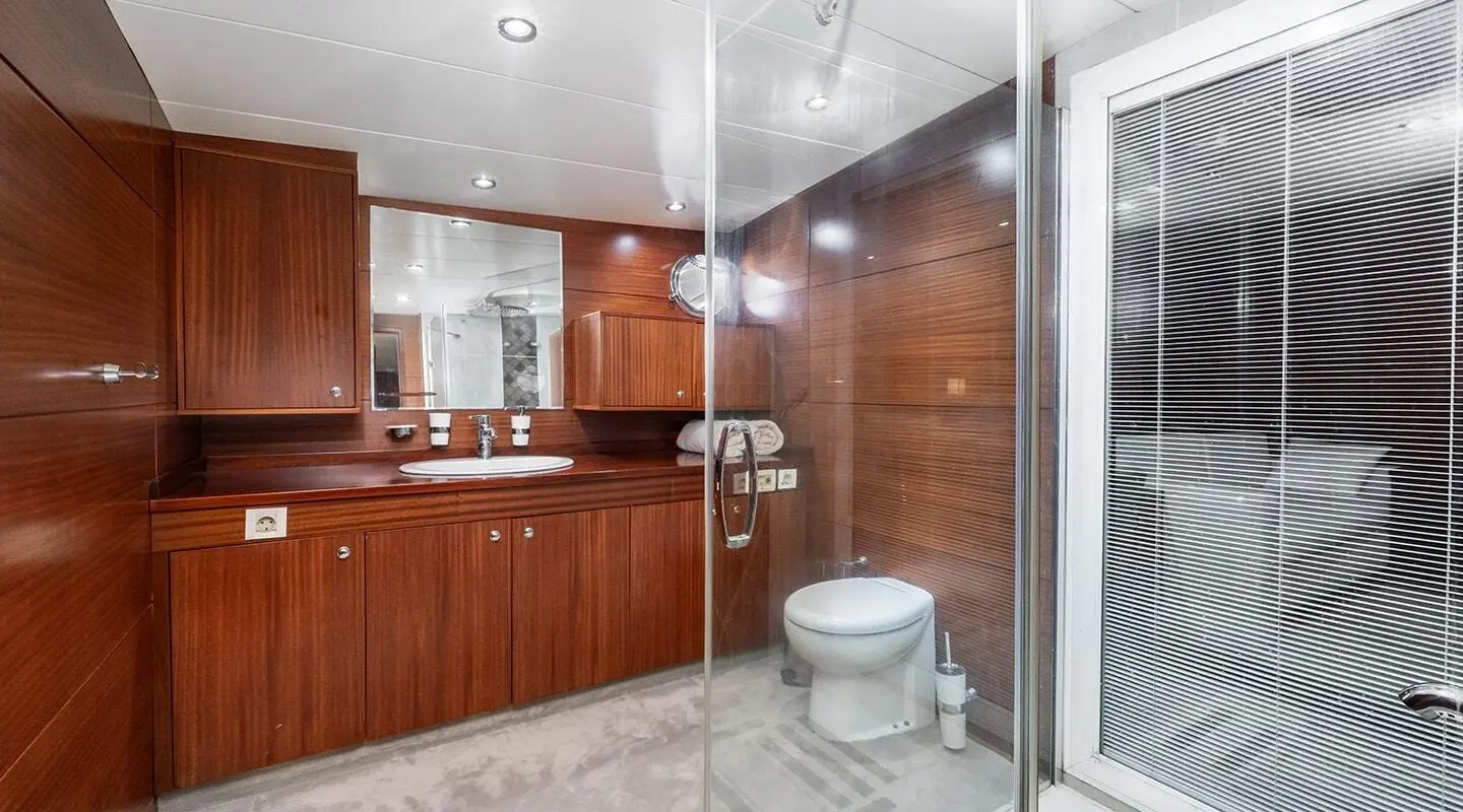 Interior of a wooden yacht bathroom with sink, mirror, toilet, and shower