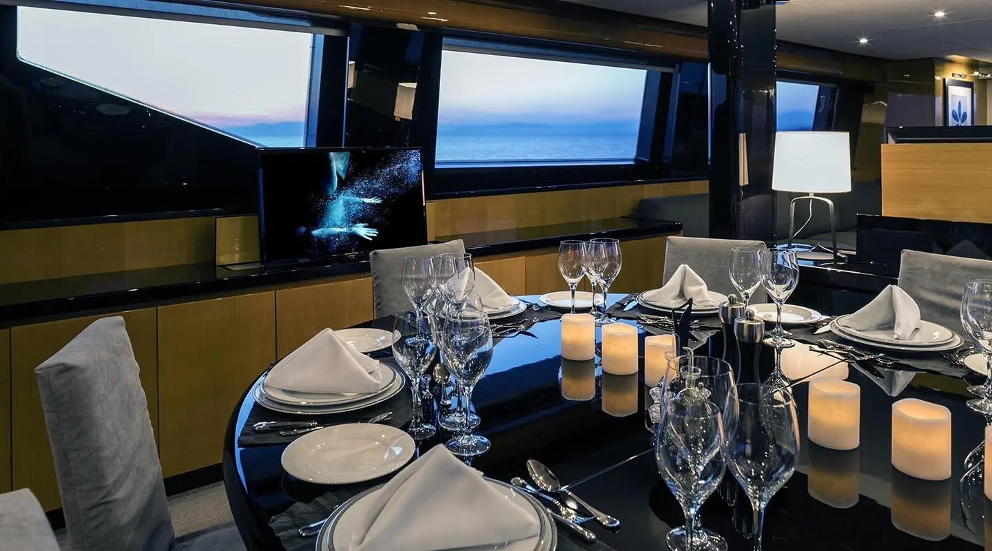 Inside dining area on a luxury yacht, sunset view through windows, table set for dining