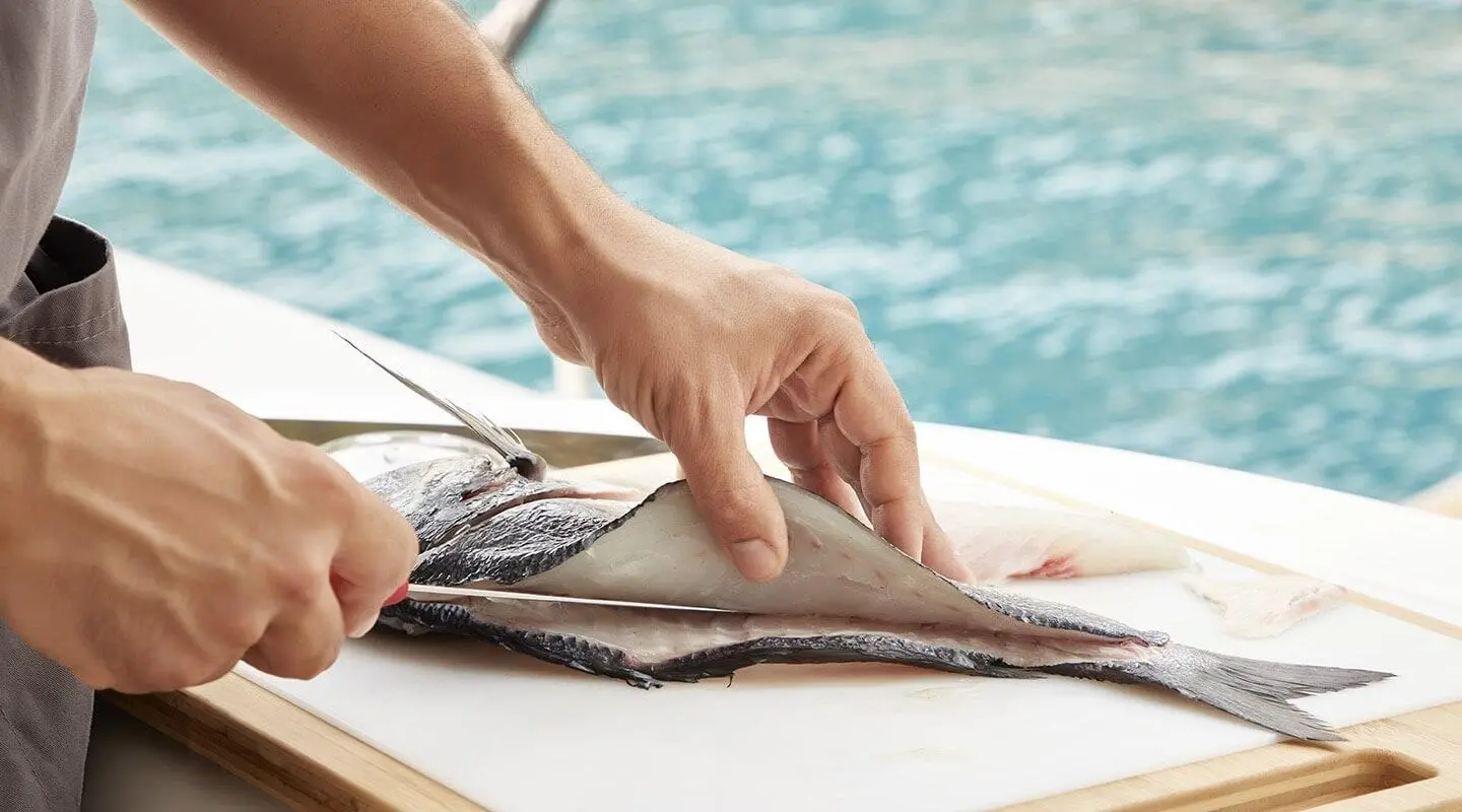 Hands filleting a fish on a wooden table beside a blue pool