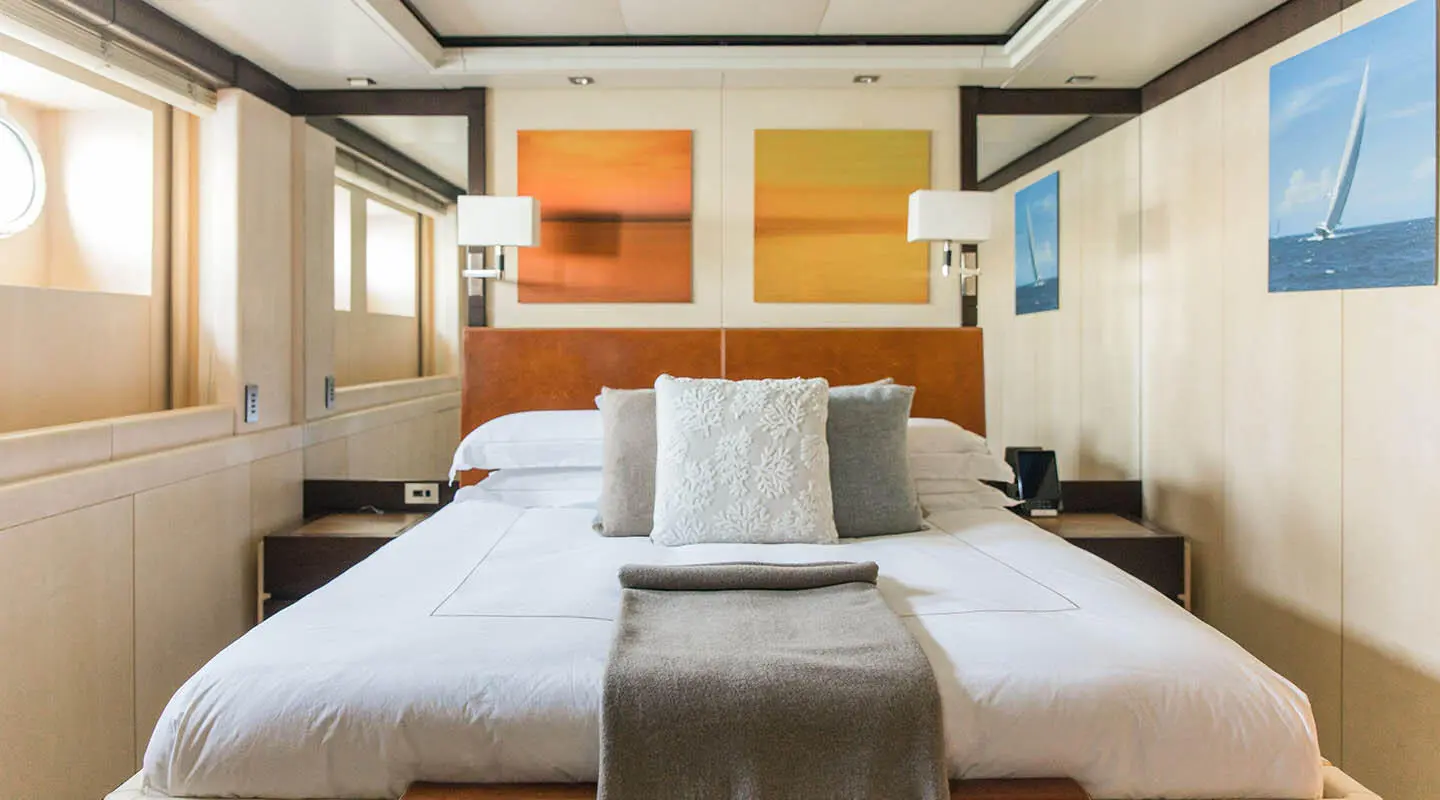 Alalya yacht bedroom with large bed, white linens, plants, and warm lighting