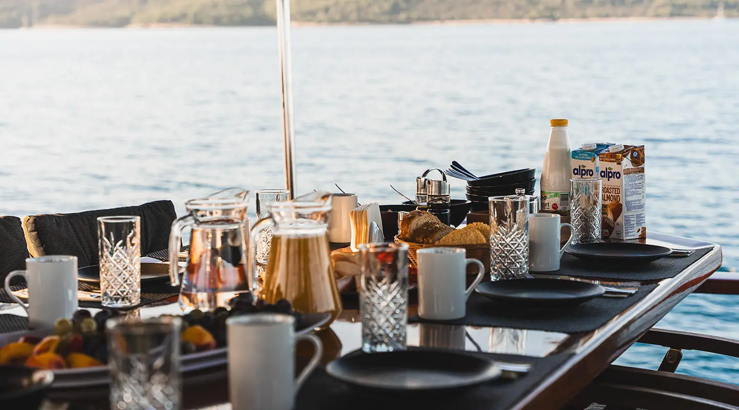 Table setup with breakfast items and drinks on a yacht deck overlooking the sea