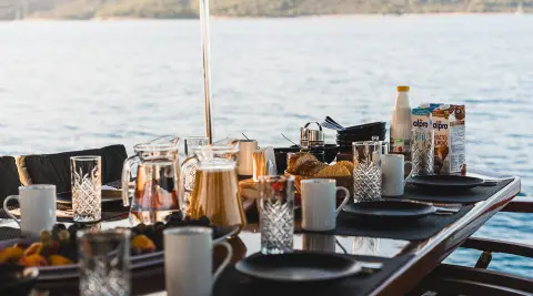 Table setup with breakfast items and drinks on a yacht deck overlooking the sea