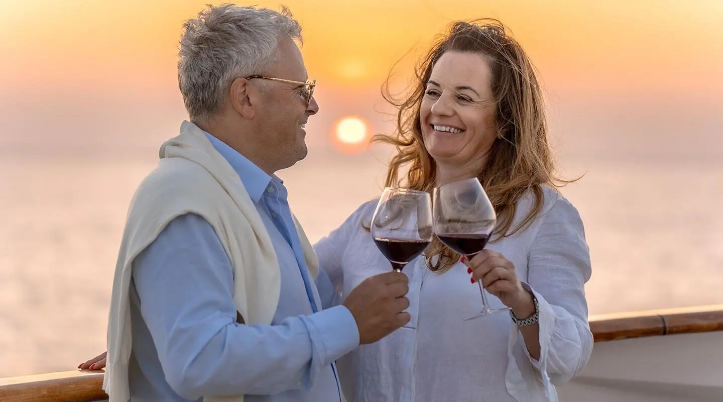 A happy couple toasting with wine glasses on a yacht during sunset
