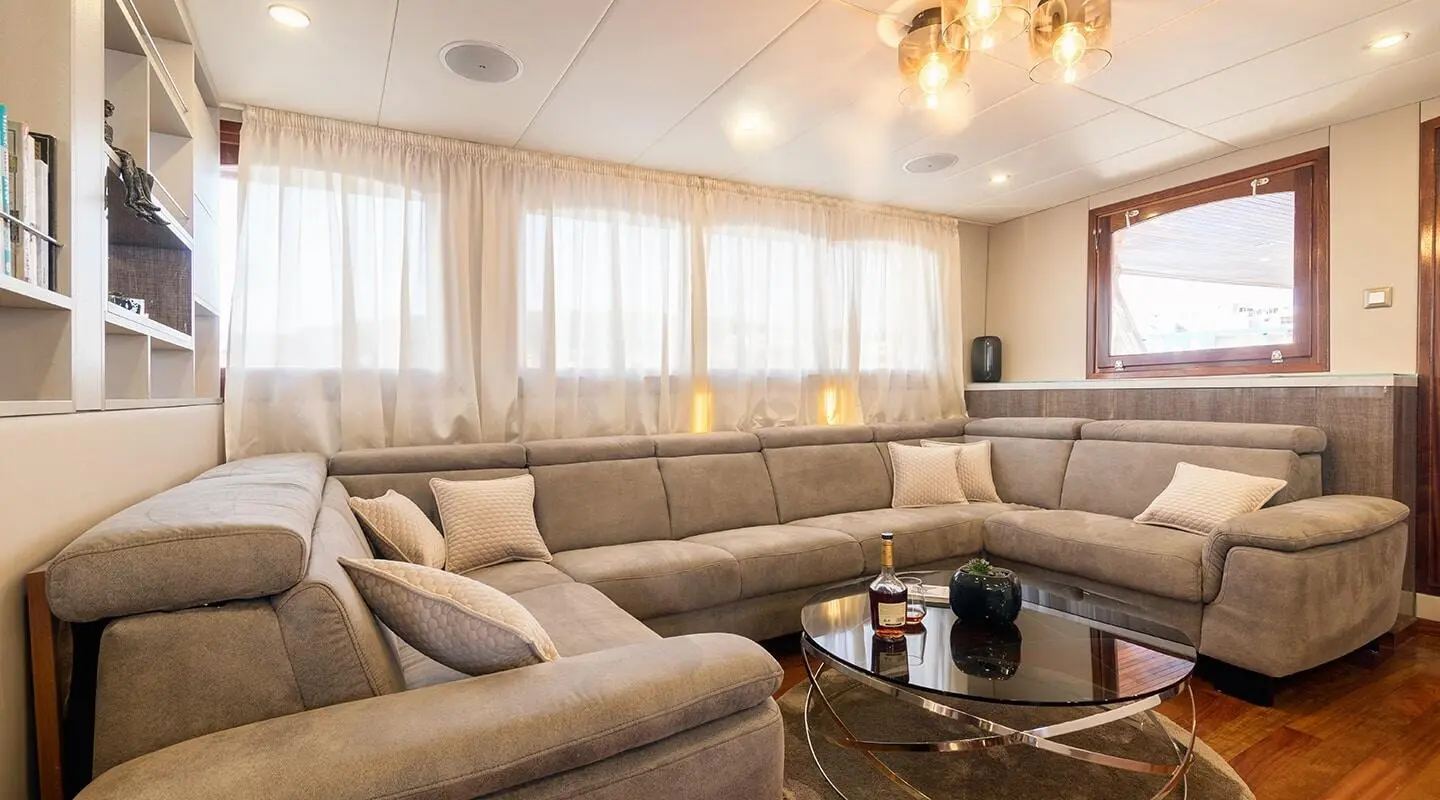 Spacious yacht Melody lounge with large windows, beige sectional seating, and glass coffee table