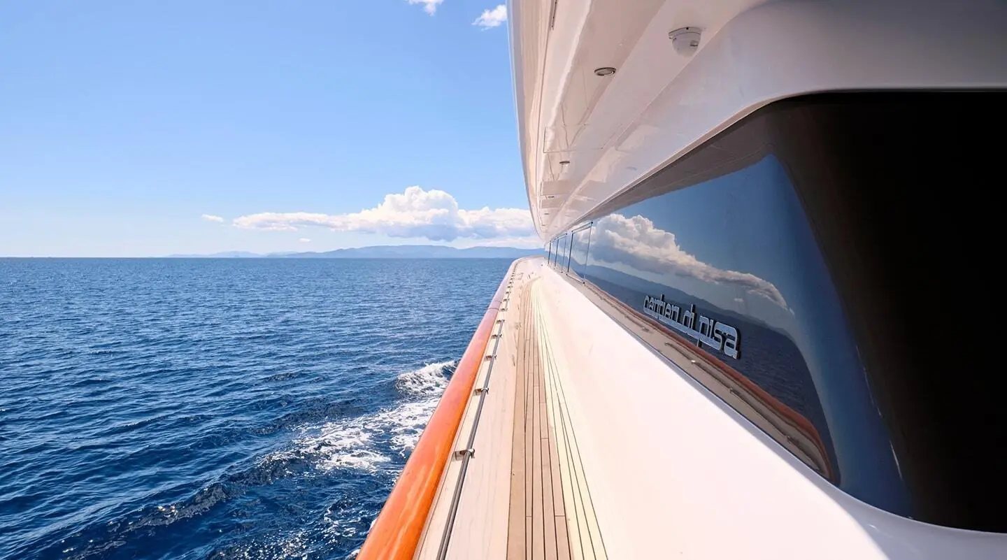 Side deck of Mobius yacht sailing on calm blue sea, sunlight on wood