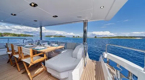 Luxurious yacht Aluminia Too deck with seating, dining area, and blue ocean view at sunset