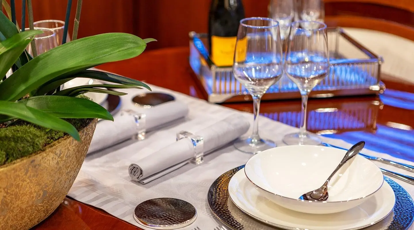 Elegant yacht dining table set with white plates, wine glasses, and silverware aboard Divine