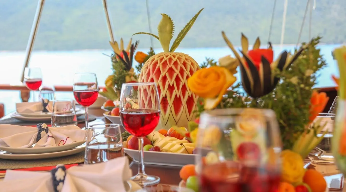 Ulucinar yacht dining on deck with red wine glasses and a carved watermelon centerpiece