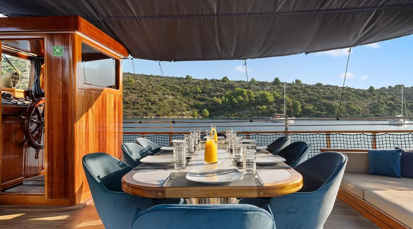 Outdoor dining on a yacht deck at sunset with a table set for six and blue water
