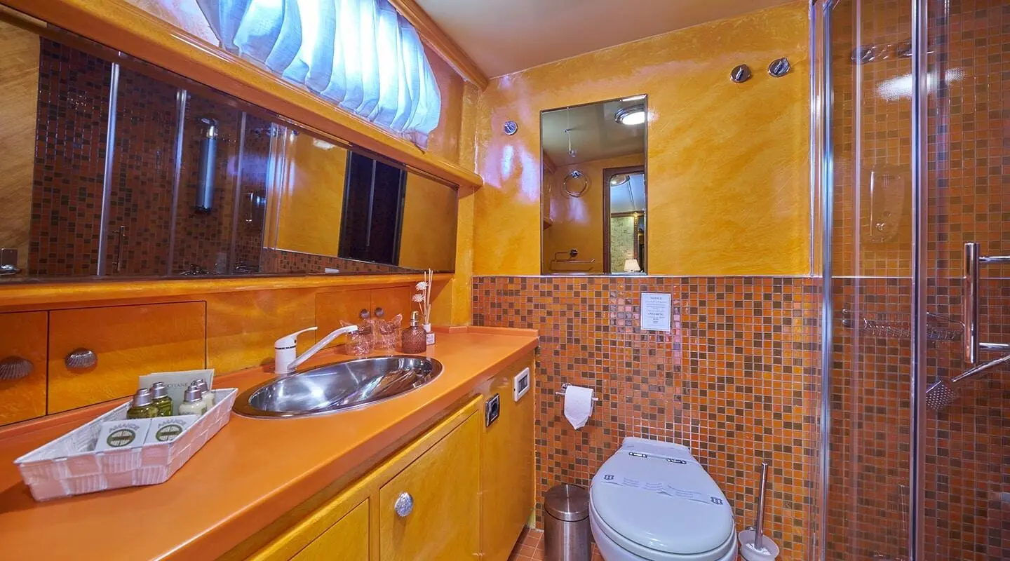 Lotus yacht interior: wooden cabinetry, sink, and yellow tiled walls with a toilet visible