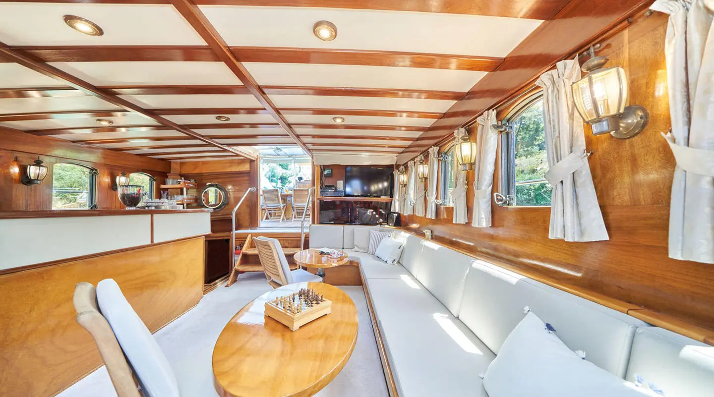 Yacht Libra interior: elegant white seating, wooden table, cabin windows at sunset