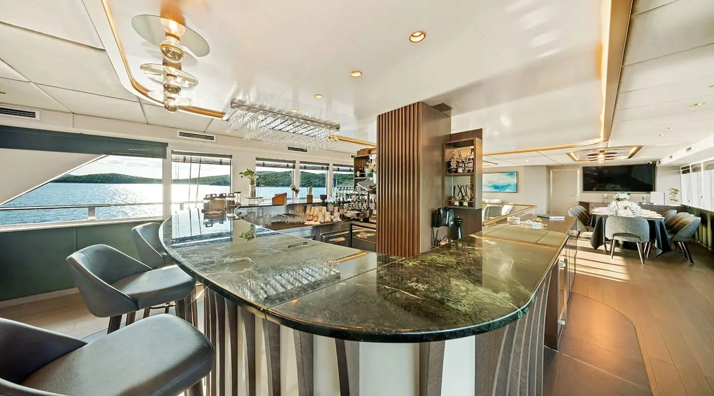 Anima Maris yacht interior with bar, seating, and panoramic windows at sunset