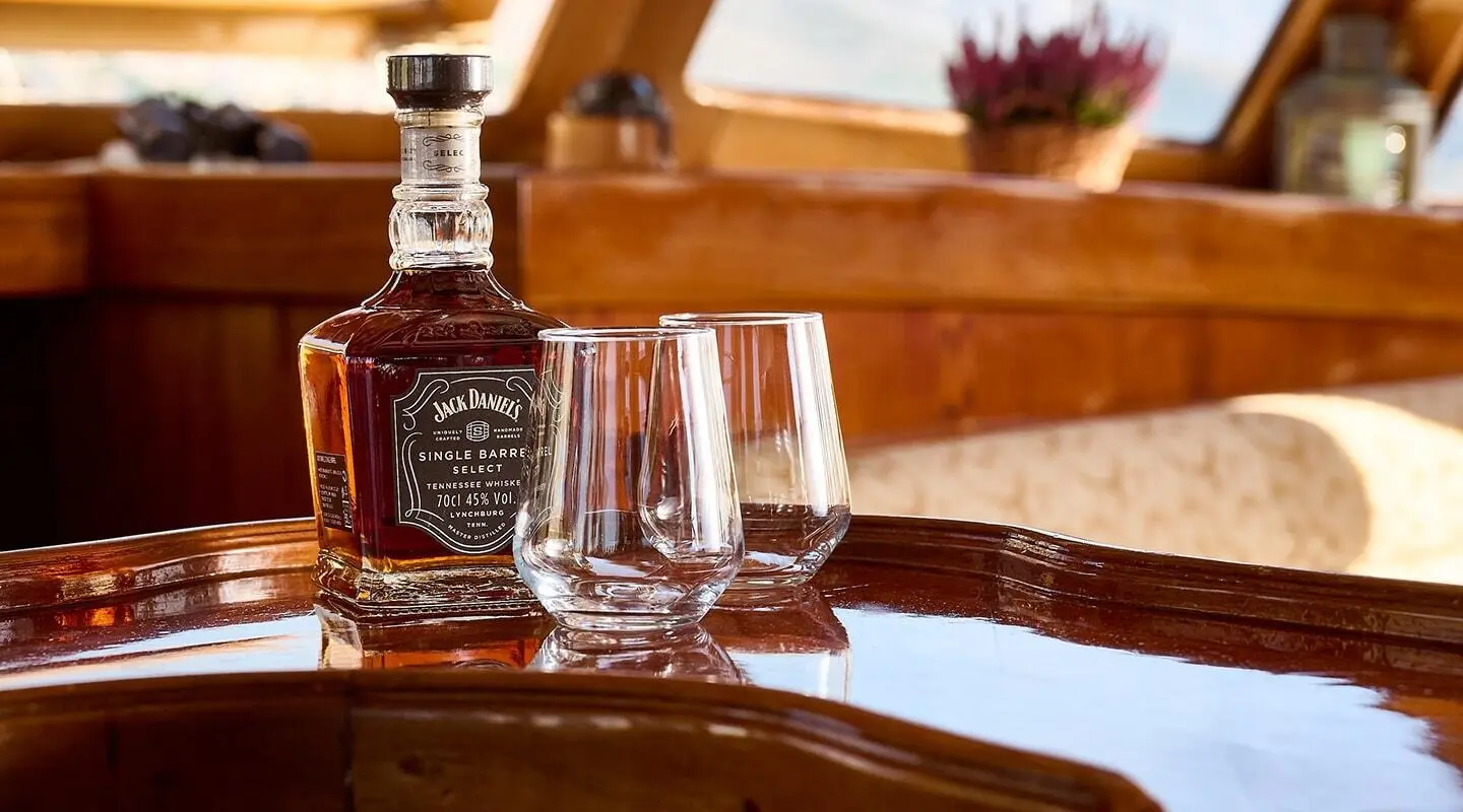 Bottle of whiskey with two glasses on a polished wooden deck